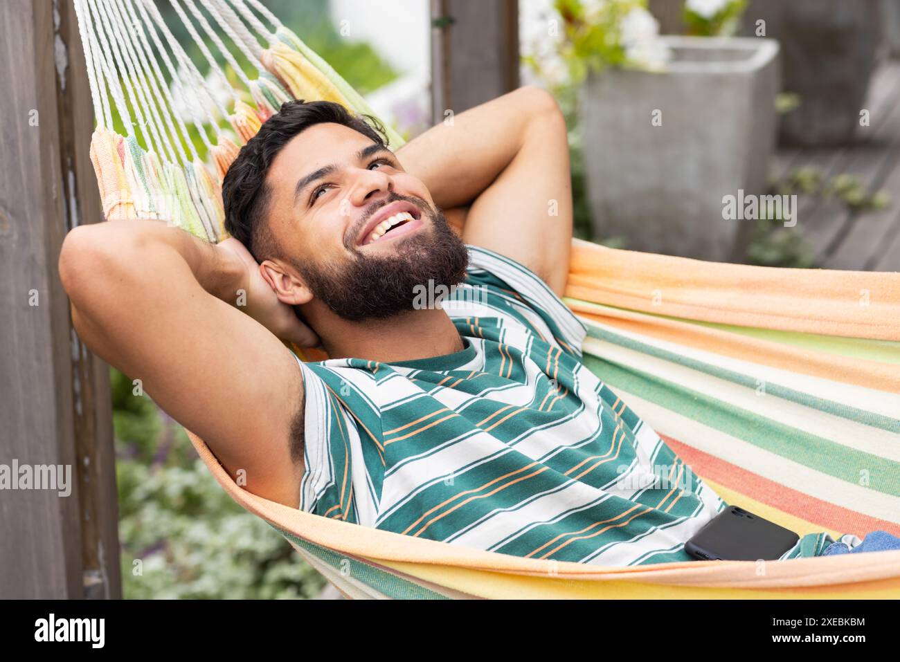 En dehors de sa maison, détente dans un hamac, homme souriant et profitant de loisirs à la maison Banque D'Images