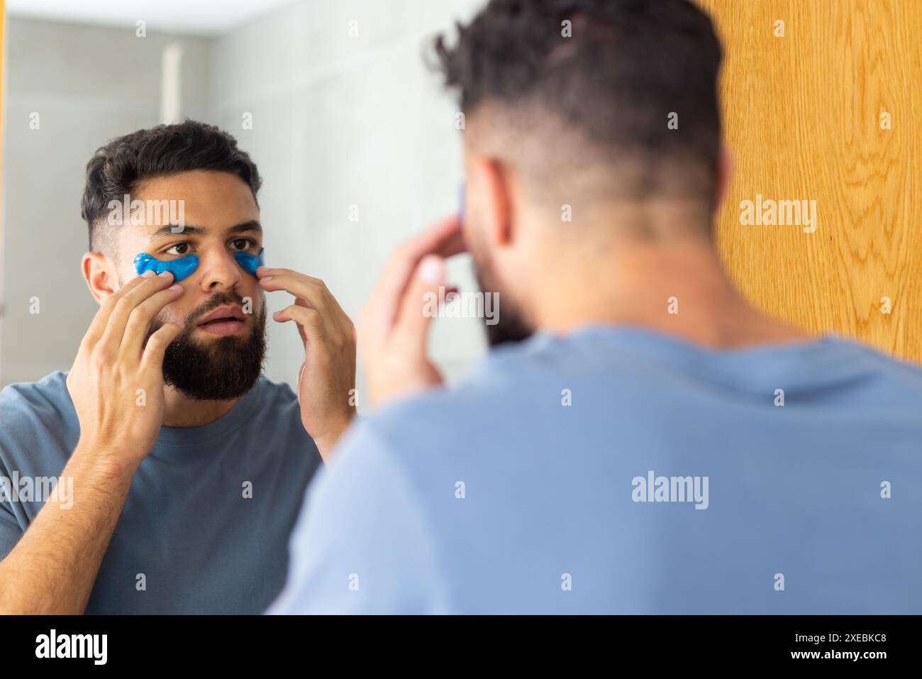 Homme appliquant des patchs sous les yeux tout en regardant dans le miroir de la salle de bain à la maison Banque D'Images