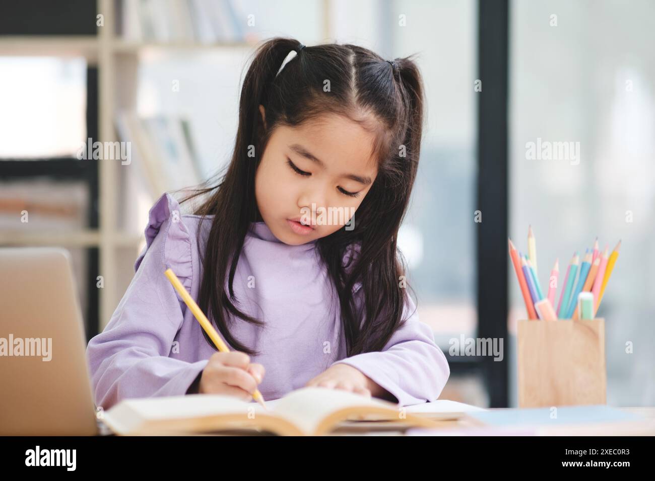 Une jeune fille est assise à un bureau avec un livre et un ordinateur portable Banque D'Images