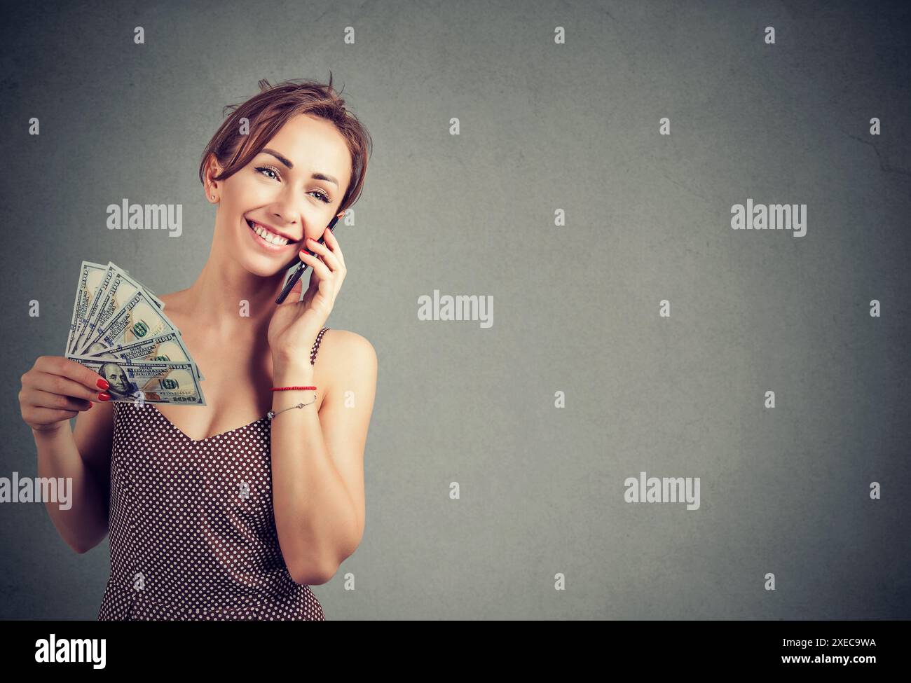 Femme souriante à l'aide du téléphone portable tenant fan de l'argent liquide Banque D'Images