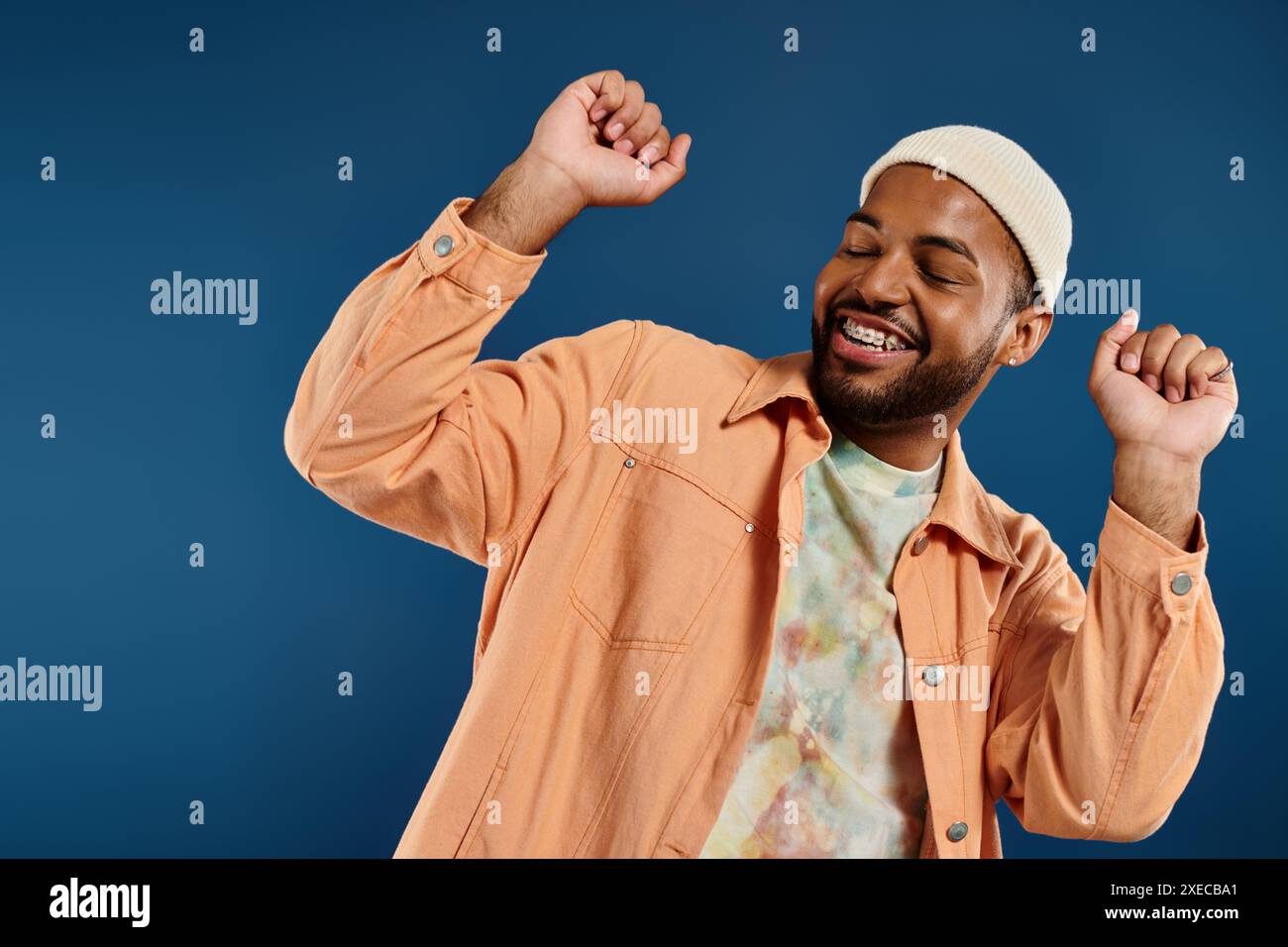 Homme afro-américain pose en chemise orange et chapeau blanc sur fond vibrant. Banque D'Images