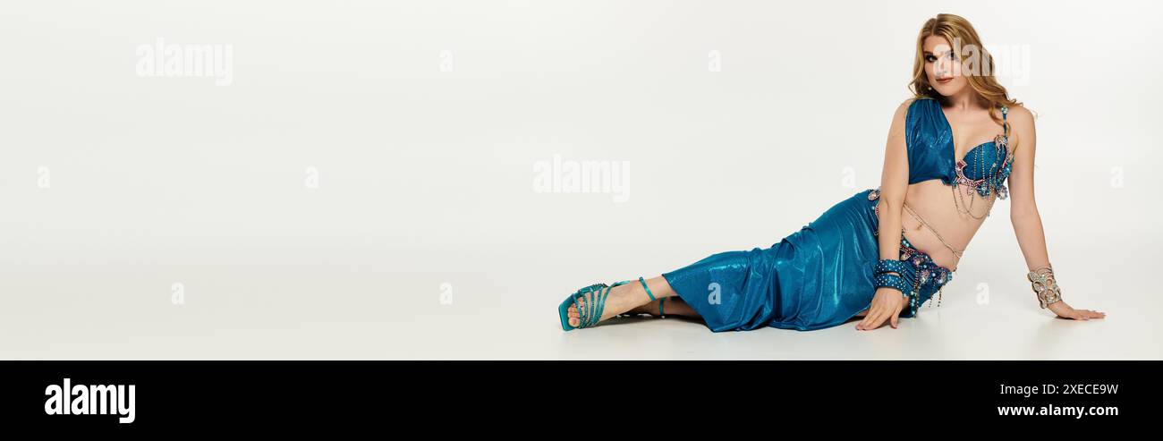 Femme gracieuse en robe bleue reposant sur le sol après la performance de danse du ventre. Banque D'Images
