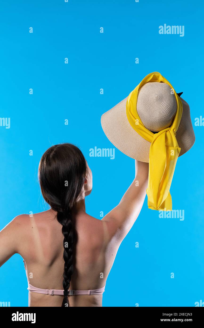Une adolescente avec une tresse leva un chapeau de plage au-dessus de sa tête. Banque D'Images