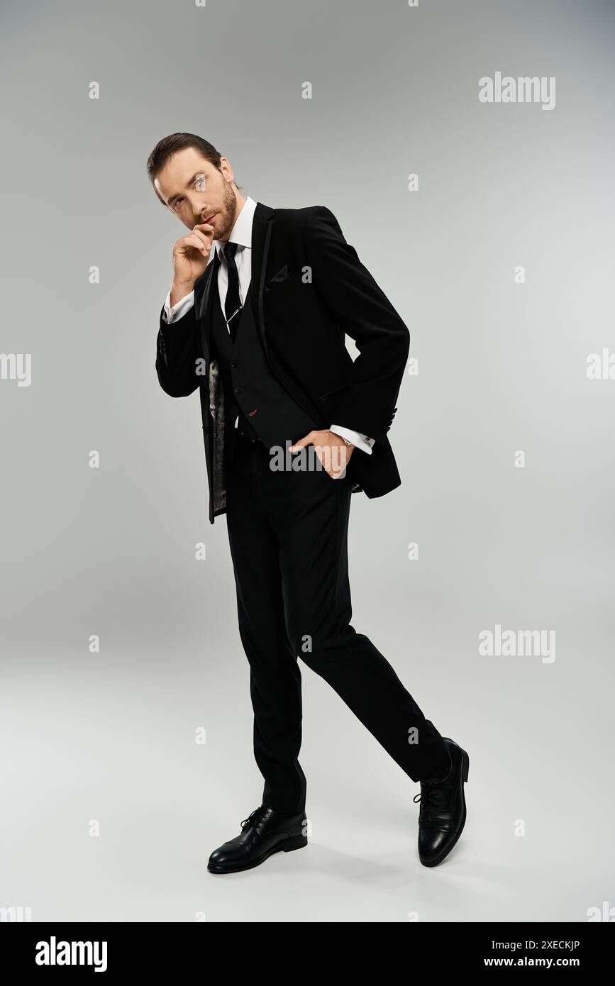 Un bel homme d'affaires barbu pose gracieusement dans un smoking sur fond de studio gris. Banque D'Images