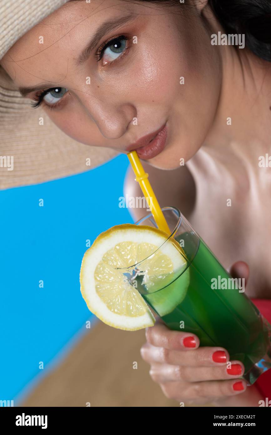 Une adolescente avec une boisson alcoolisée à la main et un grand chapeau se prélasse au soleil d'été. Banque D'Images