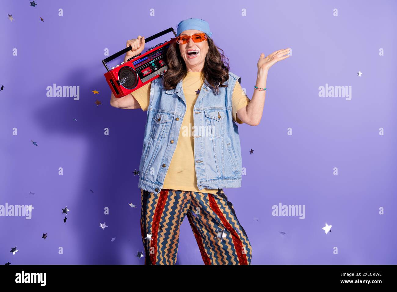 Portrait photo de la femme senior attrayante tient boombox habillé jeans élégants vêtements hipster isolés sur fond de couleur pourpre Banque D'Images