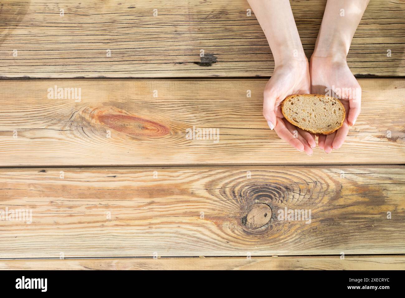 Les mains des filles tiennent une tranche de pain sur le fond d'une vieille table en bois. Une tranche de pain pour les nécessiteux. Banque D'Images