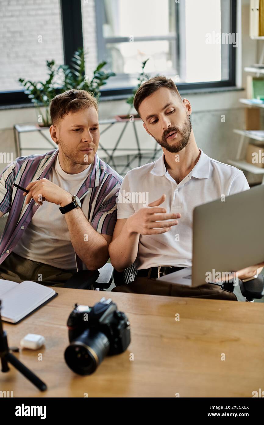 Deux hommes dans une tenue décontractée engrossés dans un ordinateur portable travaillent ensemble à une table. Banque D'Images