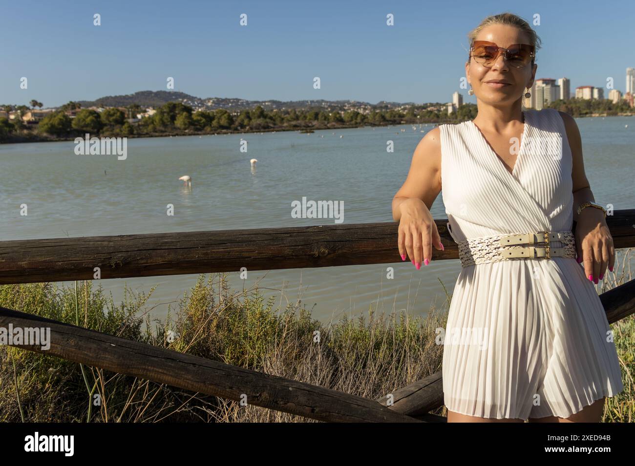Cette image capture magnifiquement une femme blonde debout au bord de l'eau. Son visage, clairement visible, rayonne un sentiment de sérénité et de paix. Banque D'Images
