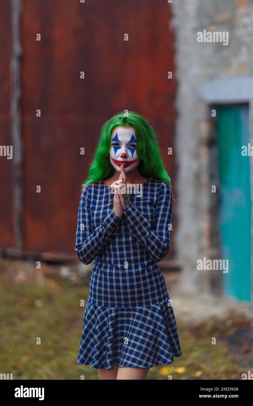 Portrait d'une fille aux cheveux verts en robe à l'entaille avec maquillage de joker sur un fond de mur en métal rouillé. Banque D'Images