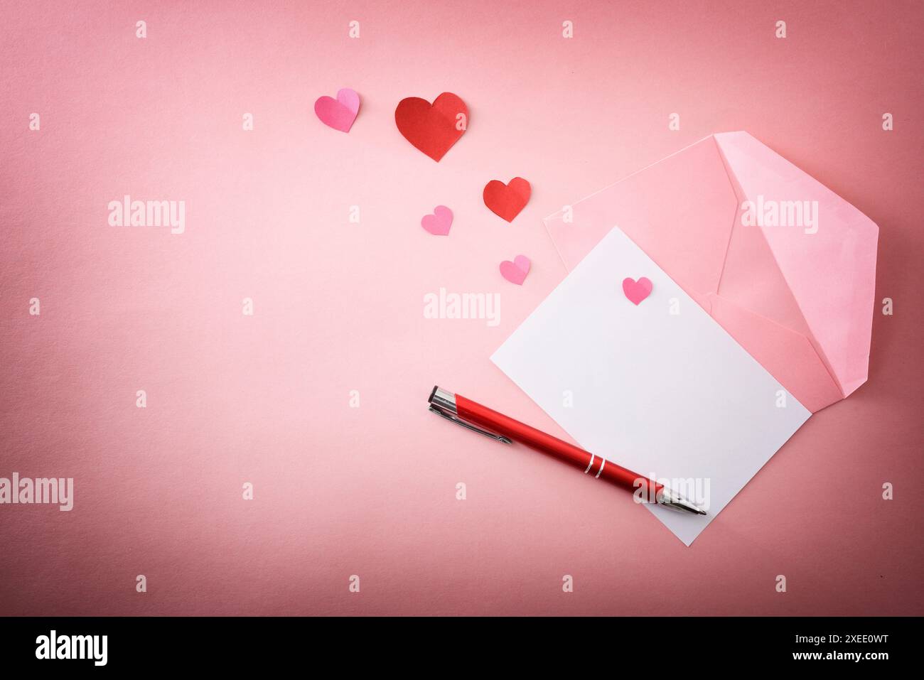 Lettre blanche sur une enveloppe rose avec stylo et des découpes de papier en forme de coeur sur une table rose avec dégradé. Vue de dessus. Banque D'Images