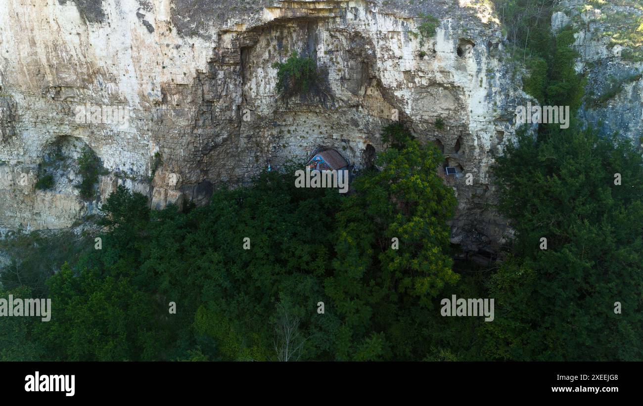 Vue aérienne d'une petite église nichée à flanc de falaise, entourée d'une forêt verdoyante Banque D'Images