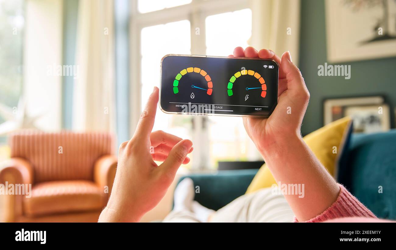 Gros plan de la femme regardant l'écran du compteur intelligent d'énergie sur le téléphone portable relaxant sur canapé à la maison Banque D'Images