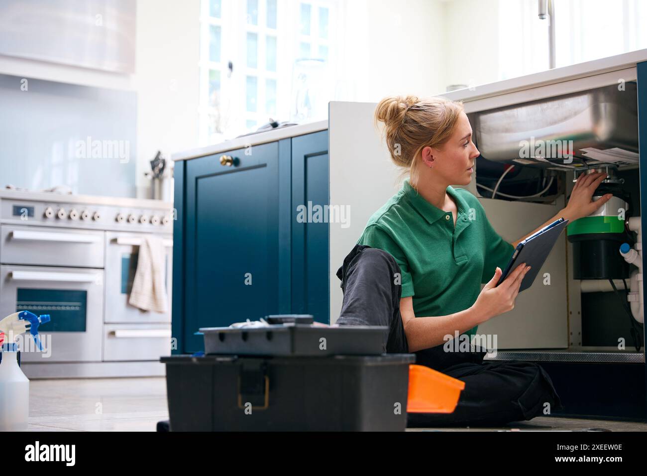 Plombier femelle avec tablette numérique fixant l'unité d'élimination des déchets dans l'évier de cuisine domestique Banque D'Images