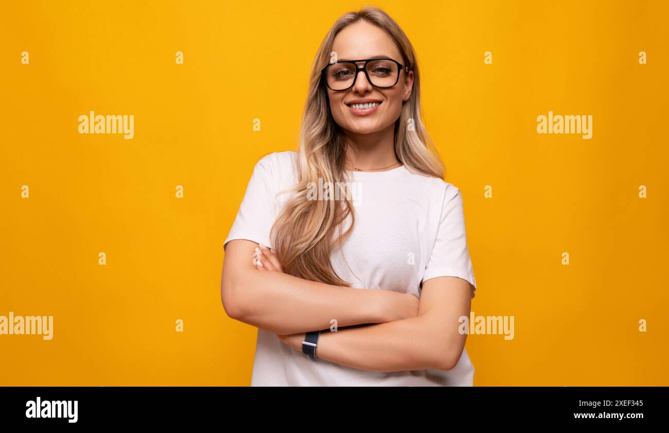 Femme blonde intelligente souriante avec une mauvaise vue portant des lunettes sur fond jaune Banque D'Images