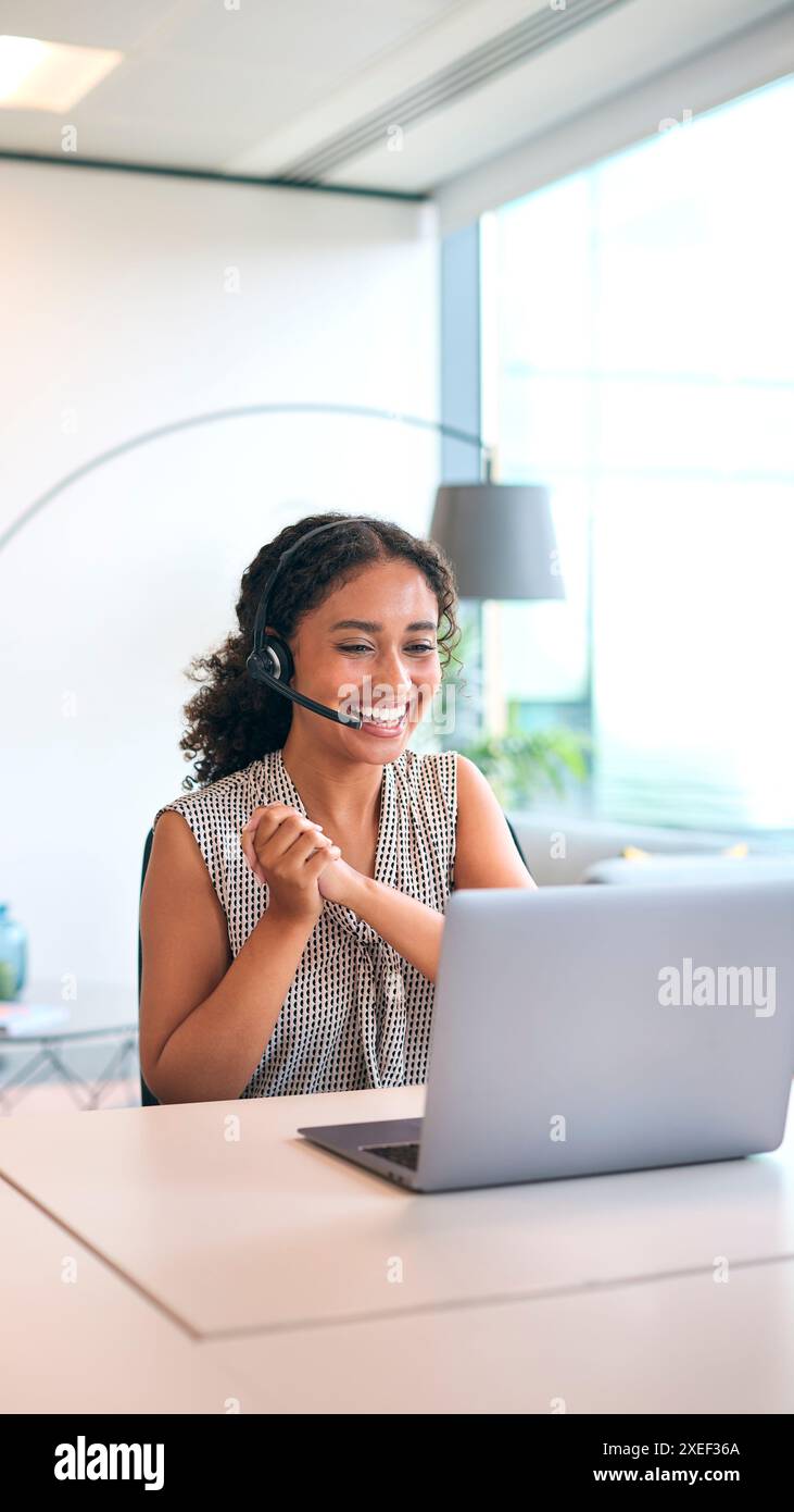 Femme portant un micro-casque assis au bureau avec un ordinateur portable célébrant les bonnes nouvelles ou atteignant l'objectif de vente Banque D'Images