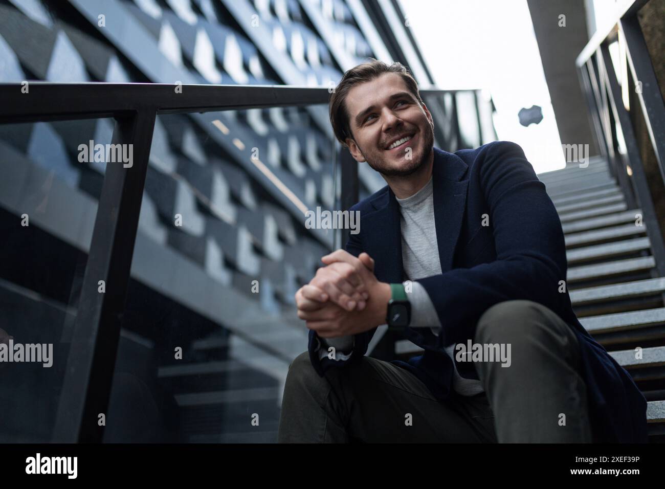 Homme indépendant souriant européen assis sur les marches d'un immeuble dans la rue Banque D'Images