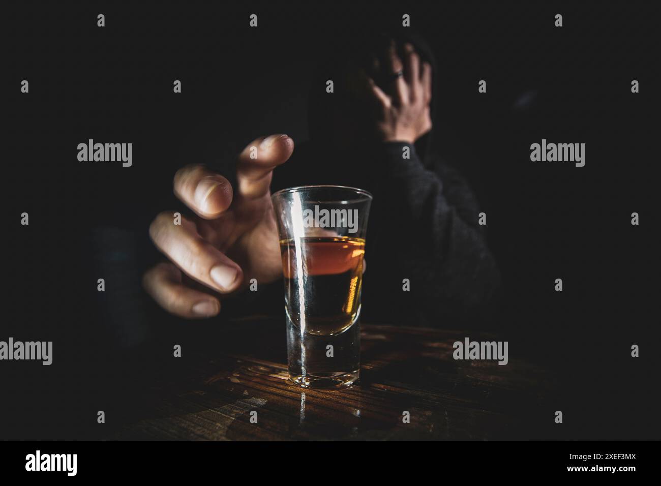 Portrait de solitaire, déprimé, jeune homme atteignant pour un coup de whisky sur le dessus d'un bar en bois. Banque D'Images