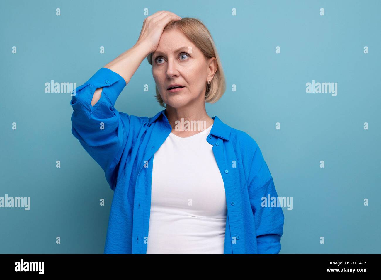 Femme mature blonde surprise dans l'incrédulité sur fond bleu avec copyspace Banque D'Images