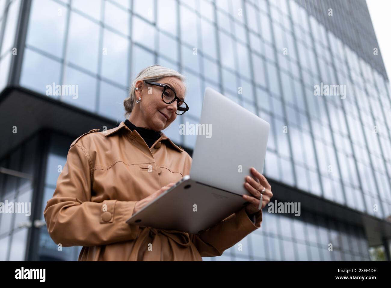 Photo horizontale du patron réussi de femme adulte mature avec ordinateur portable sur fond de bâtiment Banque D'Images