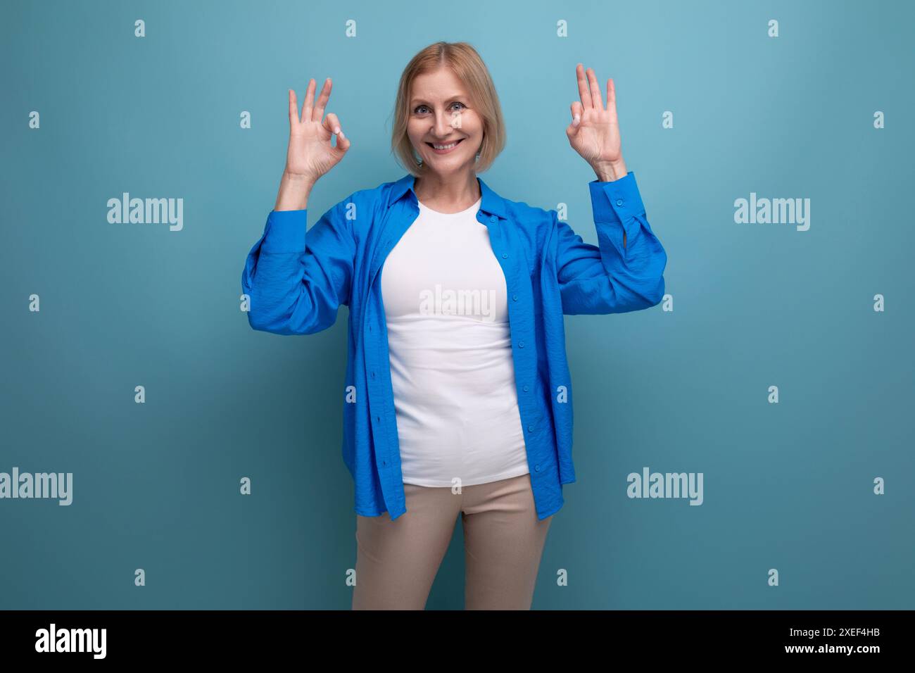 Femme d'âge moyen blonde souriante avec bob Haircut montre comme sur fond de studio Banque D'Images