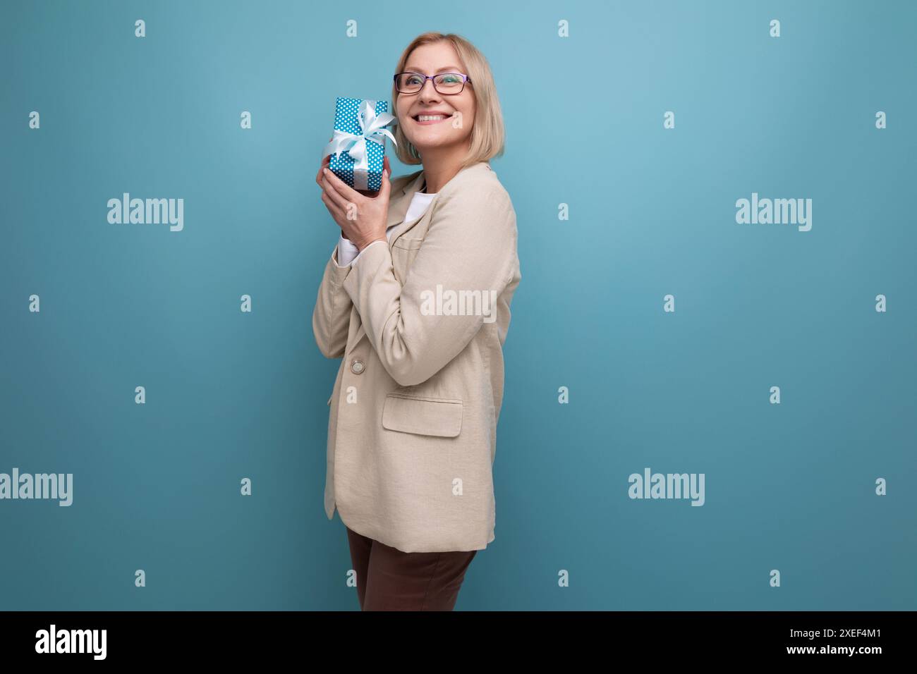 Femme mature dans une veste a reçu un cadeau pour les vacances sur un fond de studio avec espace de copie Banque D'Images