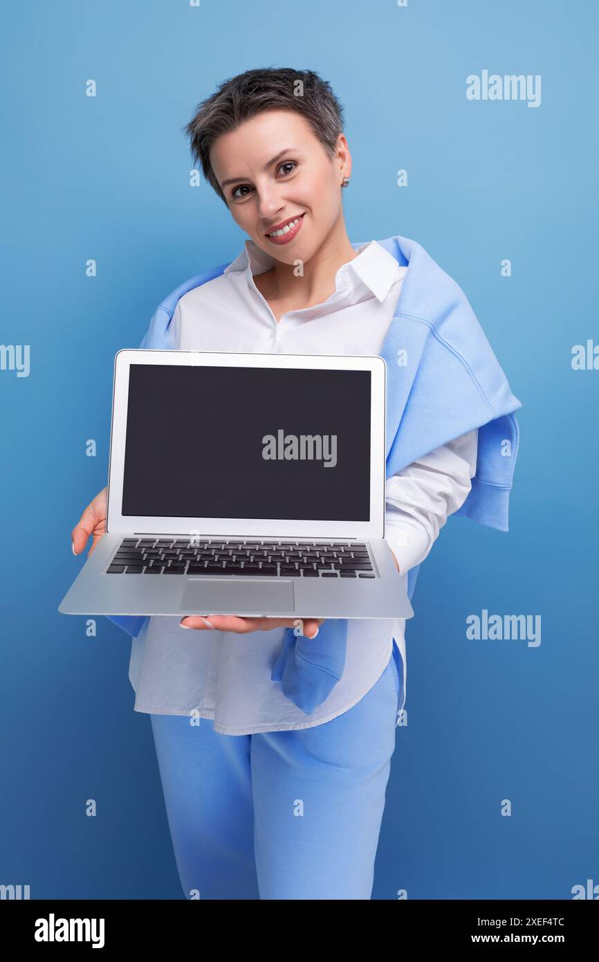 Femme indépendante élégante confiante avec maquette d'ordinateur portable sur fond de studio Banque D'Images
