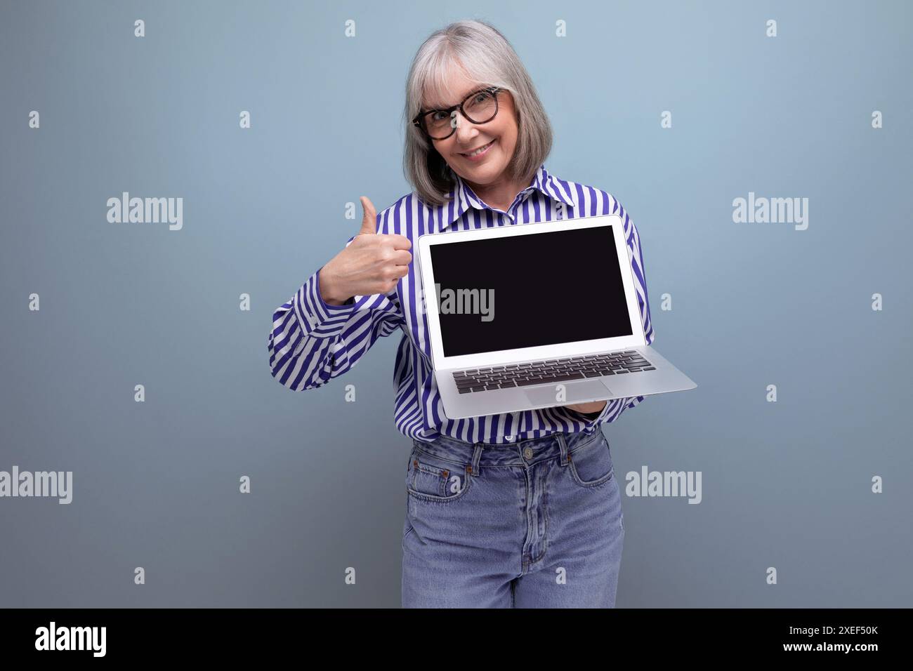 Femme mature souriante des années 60 avec les cheveux gris avec maquette d'ordinateur portable sur fond de studio lumineux Banque D'Images