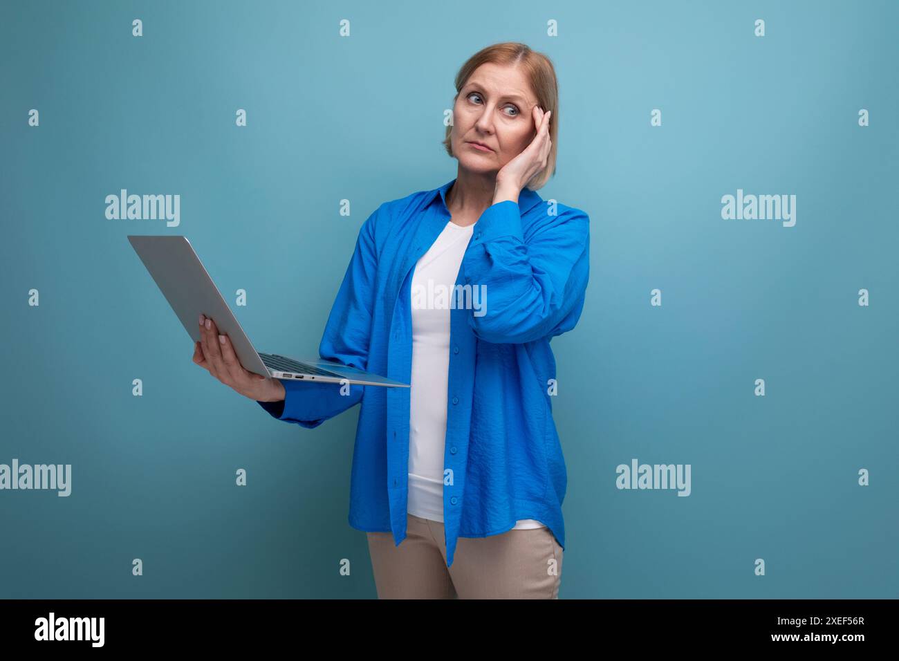 Femme d'affaires d'âge moyen travaillant comme freelance avec ordinateur portable sur fond bleu avec espace de copie Banque D'Images