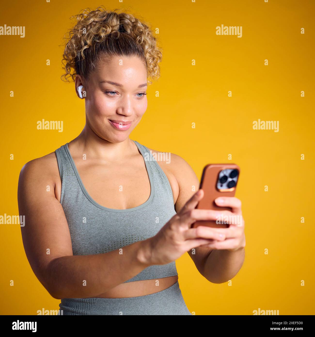 Photo studio de femme dans Gym Fitness vêtements streaming vers des écouteurs sans fil à partir d'un téléphone portable Banque D'Images