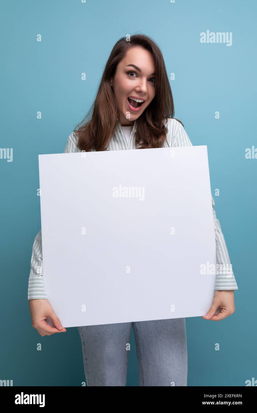Adorable femme brune de 25 ans dans une chemise et un Jean démontre un projet sur une maquette de drap blanc Banque D'Images
