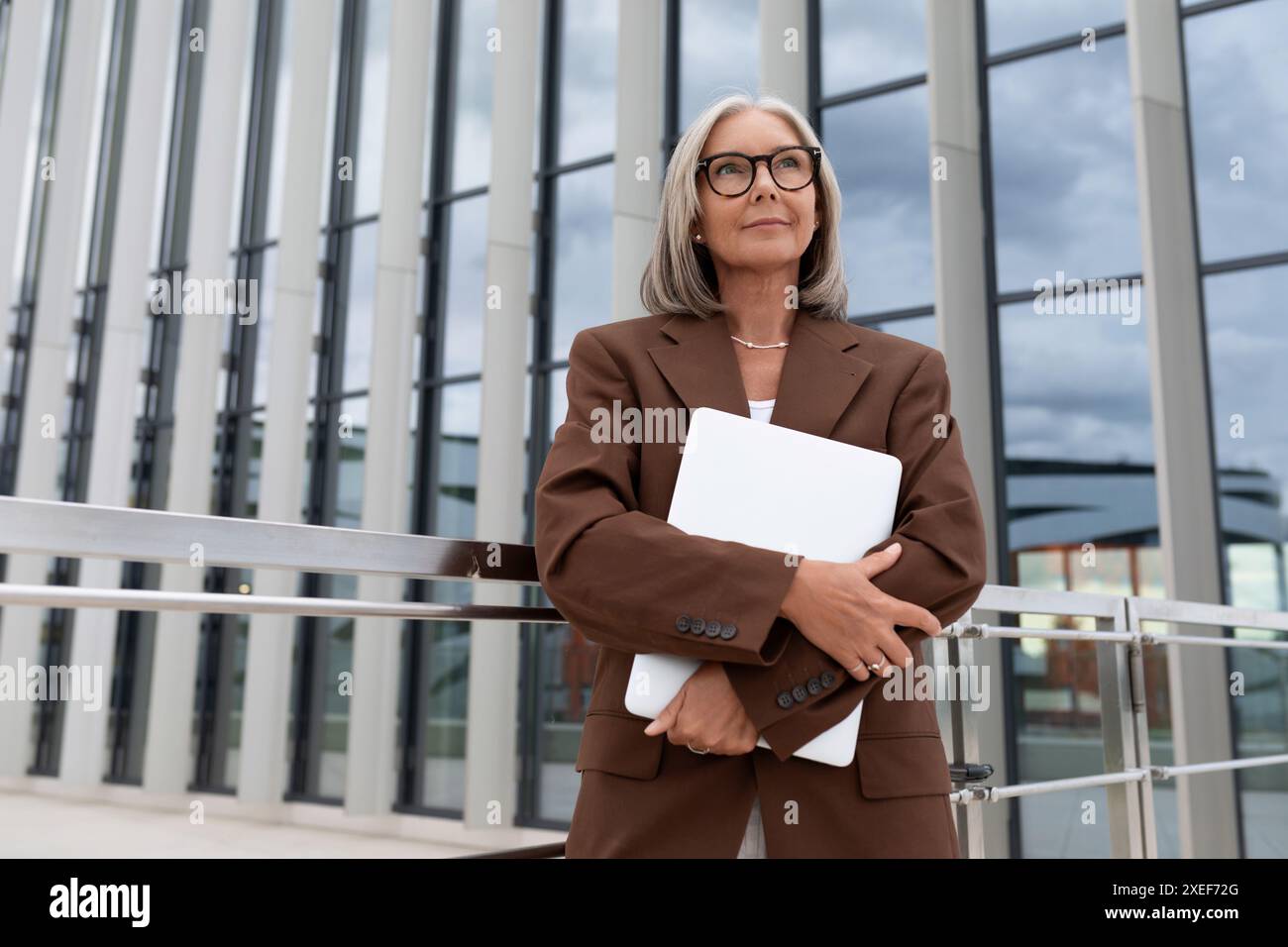 La femme d'affaires mûre aux cheveux gris mince réussie est habillée dans une veste brune élégante sur le fond du bâtiment Banque D'Images