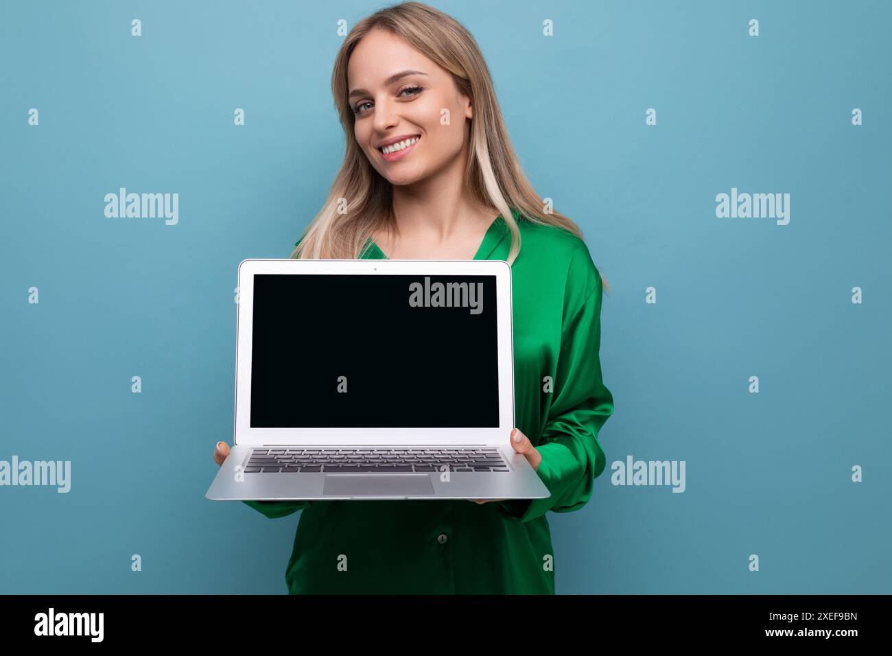 Adorable fille tenant un ordinateur portable avec un écran pour insérer un site Web sur un fond bleu lumineux Banque D'Images