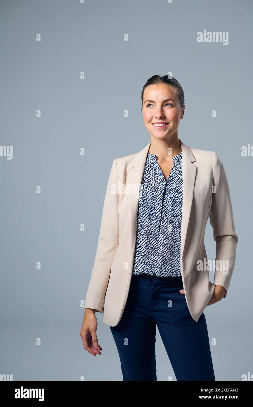Studio Portrait de femme d'affaires souriante portant costume avec la main sur la hanche sur fond gris Banque D'Images