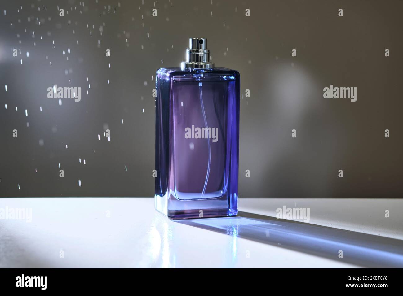 Vaporisateur de parfum dans une bouteille violette sur un fond sombre. Banque D'Images