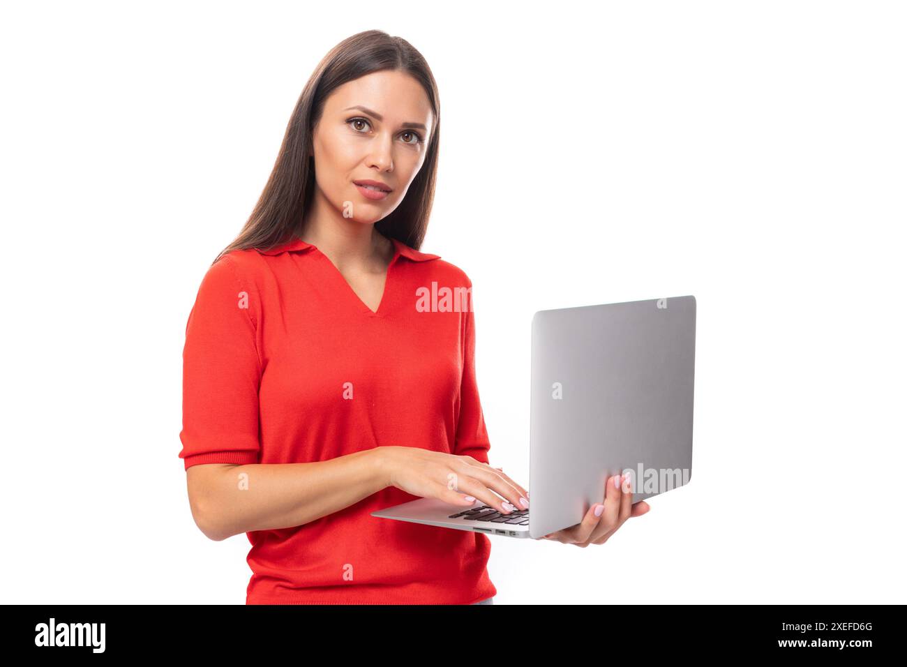 Jeune femme brune vêtue d'un t-shirt rouge tient un ordinateur portable gris dans ses mains sur un fond blanc Banque D'Images