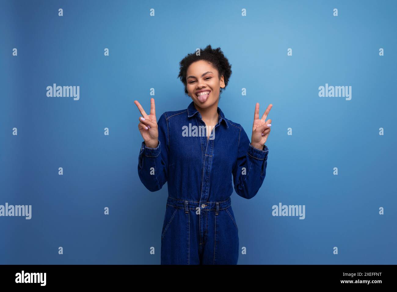 Une jeune femme latine brune avec des cheveux afro attachés dans un chignon est habillée dans un costume en denim élégant bleu Banque D'Images