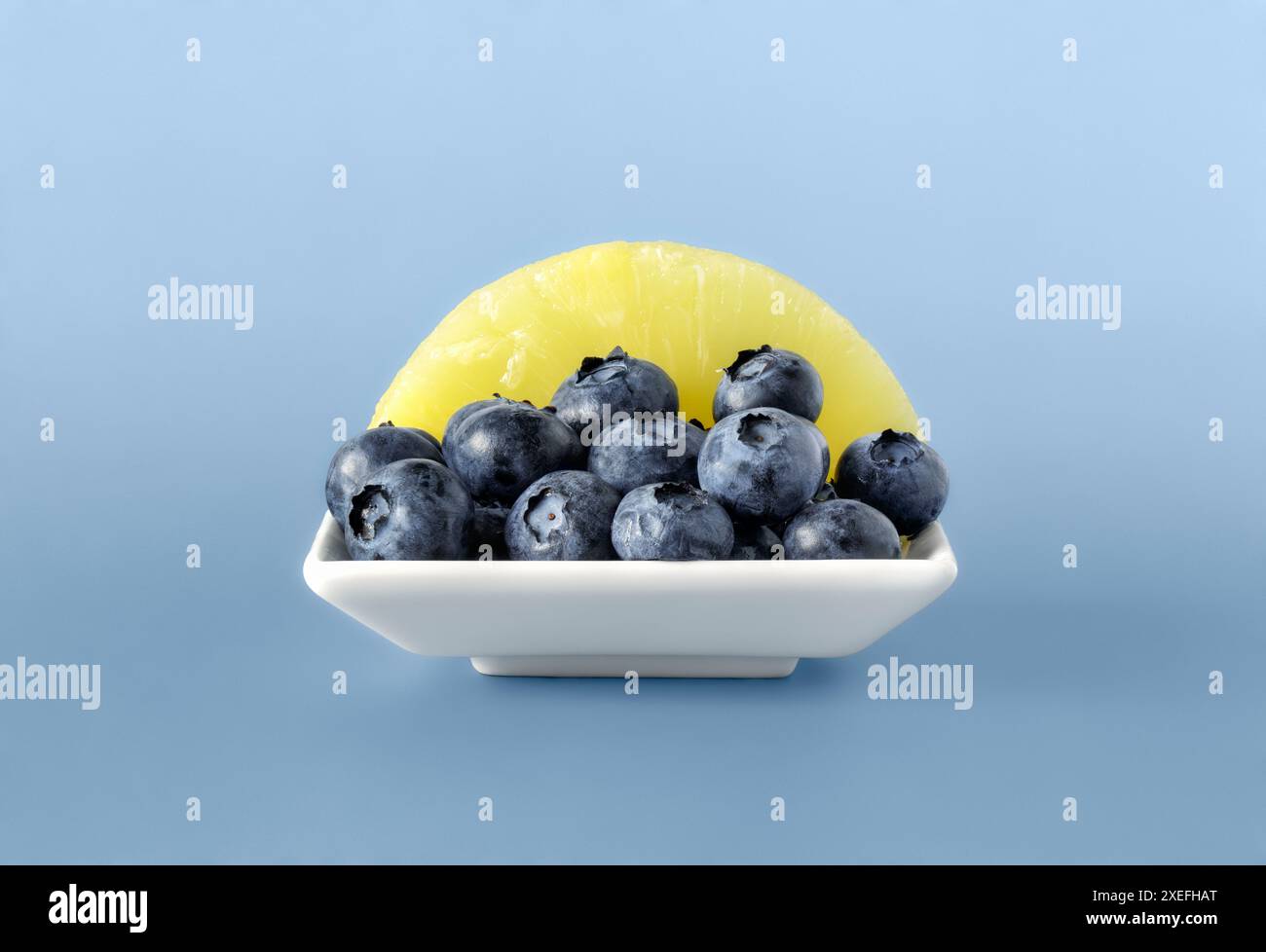 Bol carré blanc rempli de baies bleues fraîches et d'une tranche d'ananas Banque D'Images