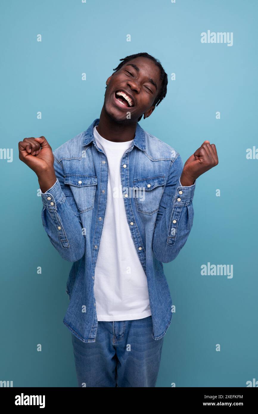 Heureux homme africain joyeux avec les cheveux bouclés dans un look décontracté éprouve des émotions agréables Banque D'Images
