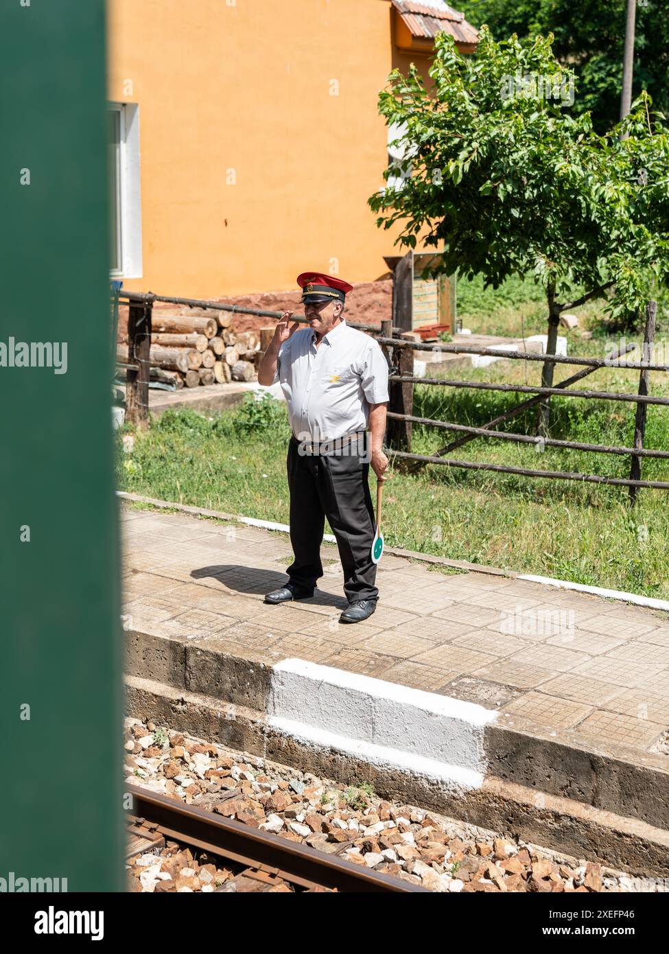 Conducteur de train en uniforme tenant une pagaie de signalisation attendant l'arrivée du train à la gare rurale Banque D'Images
