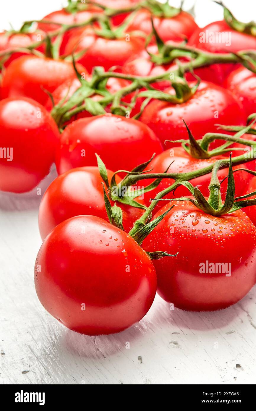 Un bouquet de tomates cerises mûres avec des gouttes d'eau sur une surface en bois blanc. Gros plan de tomates cerises. Orientation verticale de la photo. Banque D'Images