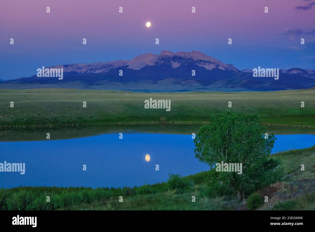 coucher de pleine lune dans un ciel avant l'aube au-dessus de la crête en dents de scie reflétée dans un étang de prairie près de choteau, montana Banque D'Images