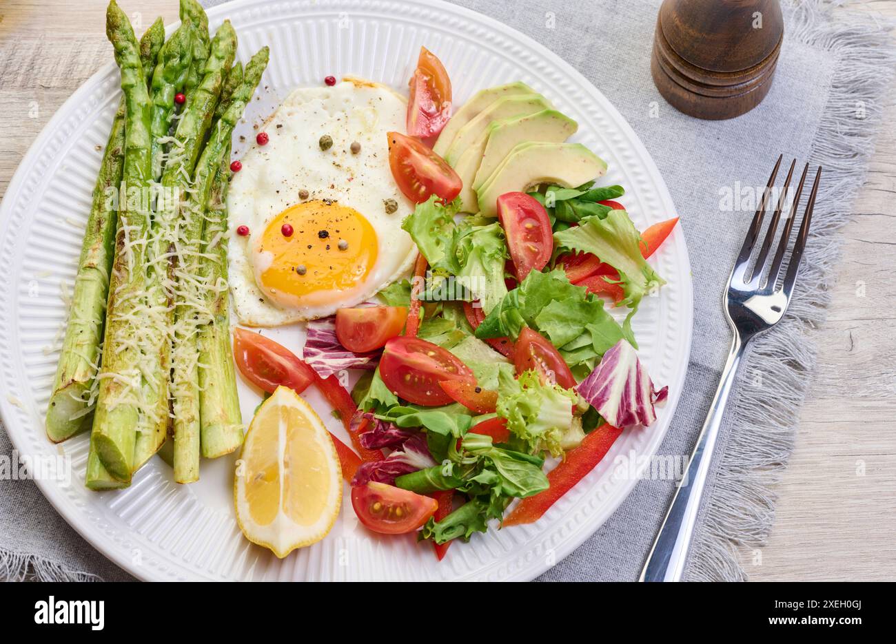 Assiette ronde avec asperges cuites, oeuf frit, avocat et salade de légumes frais sur la table Banque D'Images