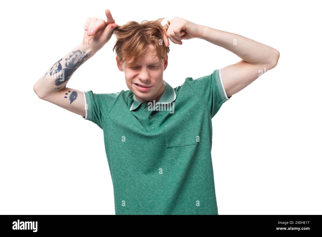 Jeune homme européen élégant avec les cheveux roux avec un tatouage sur son avant-bras porte un t-shirt vert touche ses cheveux Banque D'Images
