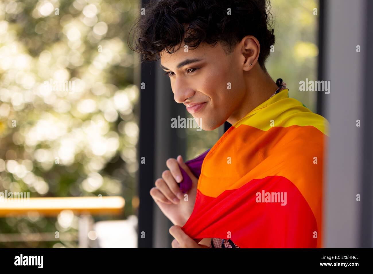 Jeune femme transgenre souriante tenant le drapeau arc-en-ciel, célébrant la fierté LGBTQ+ à la maison Banque D'Images