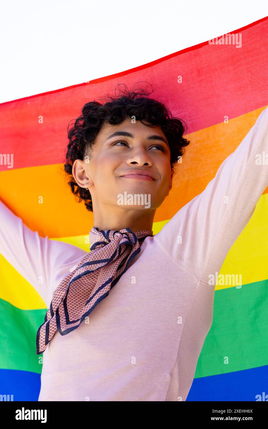Tenant le drapeau arc-en-ciel, jeune homme souriant et célébrant la fierté LGBTQ+ en plein air Banque D'Images