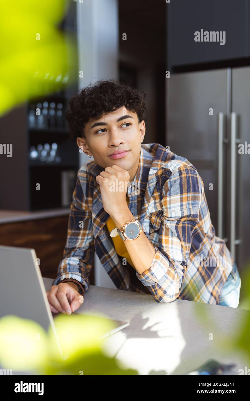 Pensant profondément, adolescent garçon en chemise à carreaux appuyé sur le comptoir de la cuisine. Contemplation, réflexion, décontracté, intérieur, style de vie, plan de travail Banque D'Images