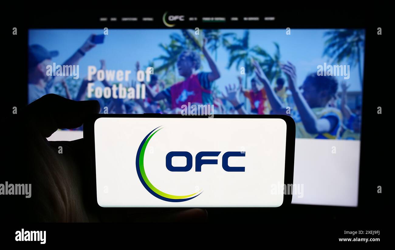 Personne tenant un téléphone portable avec le logo de l'association Oceania Football Confederation (OFC) en face de la page web. Concentrez-vous sur l'affichage du téléphone. Banque D'Images