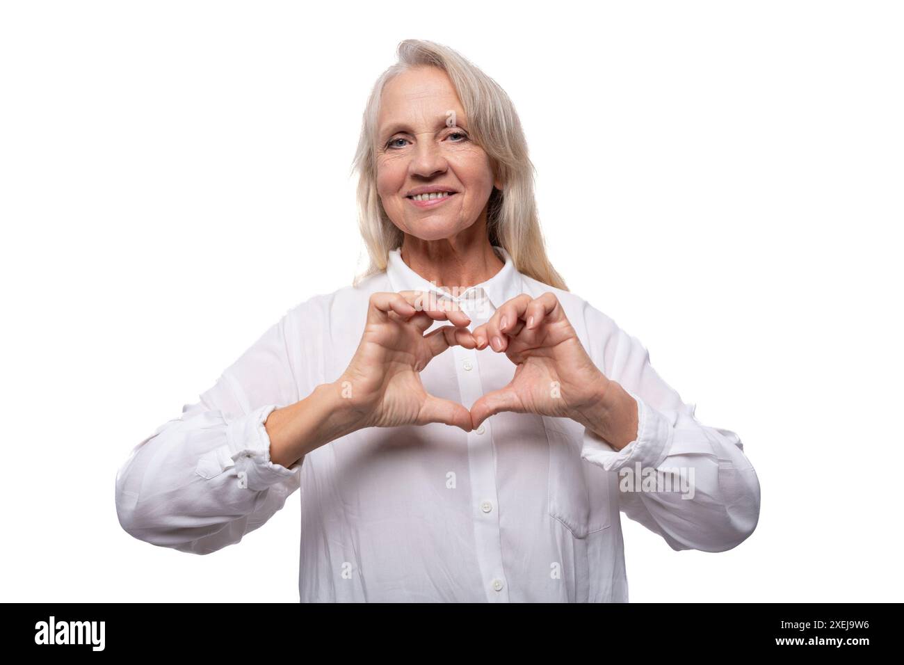 Portrait d'une gentille femme d'affaires âgée avec les cheveux gris dans une chemise montrant un coeur avec ses mains Banque D'Images