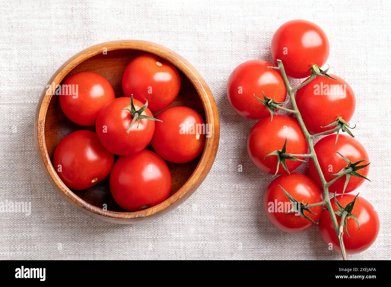 Tomates cerises rouges dans un bol en bois sur tissu de lin. Fraîche, type mûr de tomates cocktail petites et rondes, sur le côté gauche toujours sur la vigne. Banque D'Images
